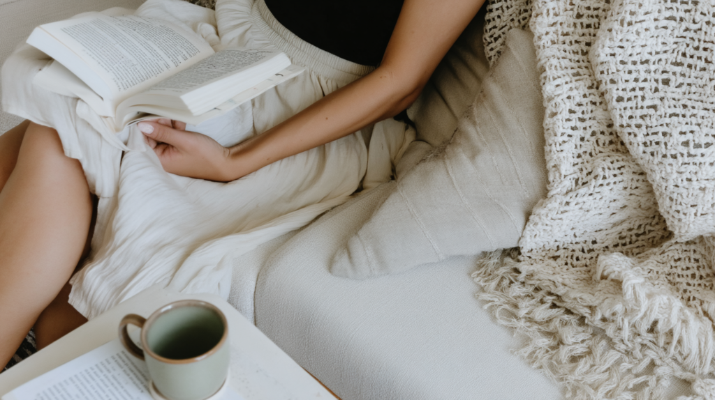 a woman reads a book on a cozy sofa with a mug of tea nearby