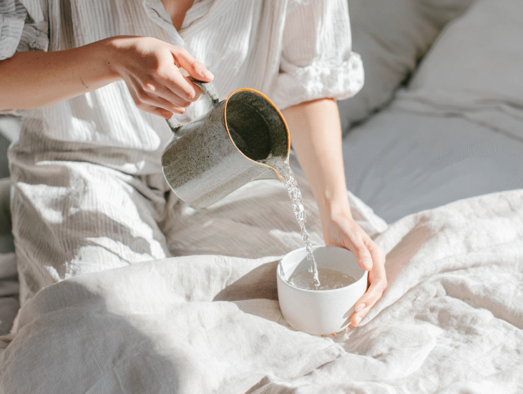 a woman pours water into a cup from a metal pitcher in the sunlight