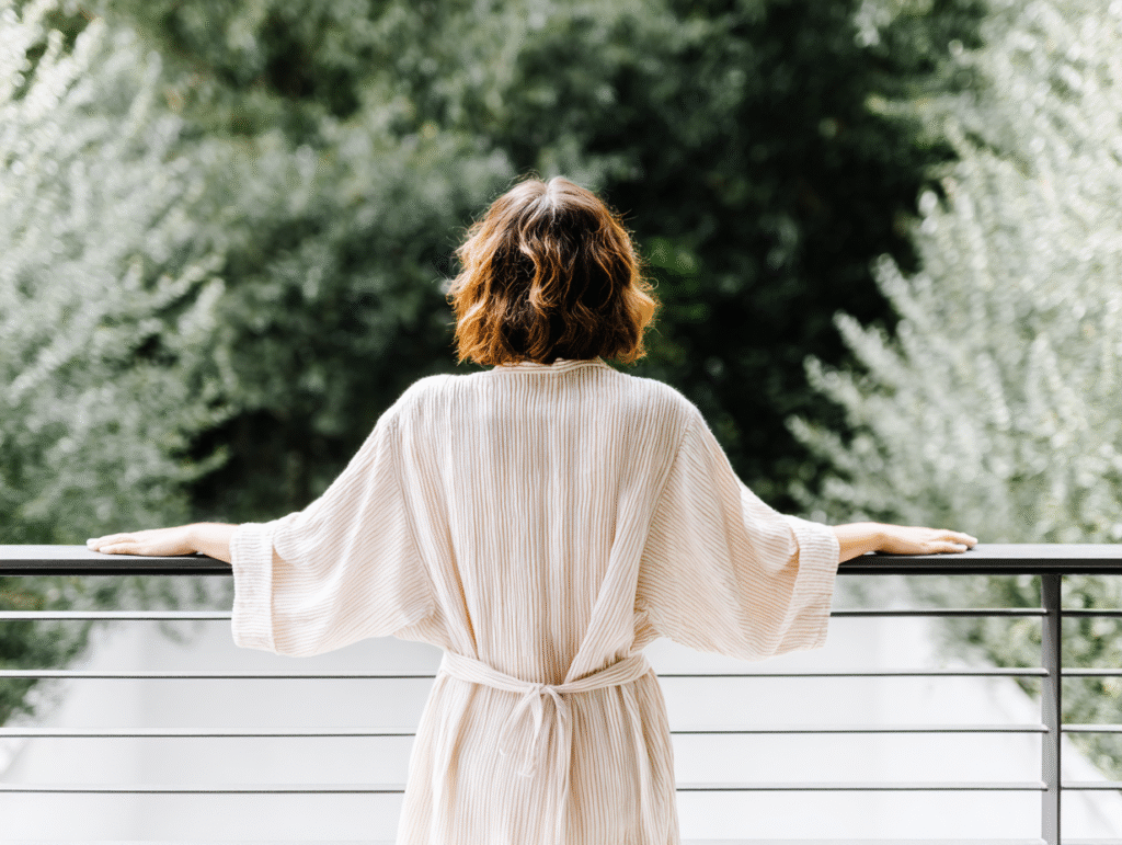 a woman stands at her balcony in a robe overlooking her garden
