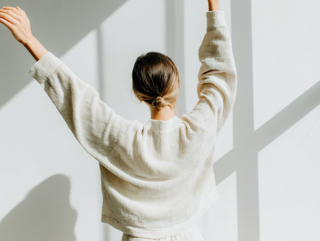 a woman stretches her arms overhead in the bright sunlight