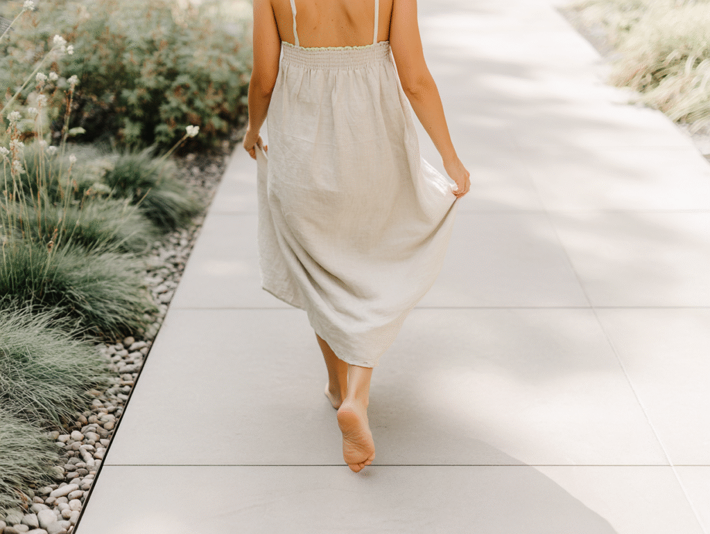a woman in a linen dress walk barefoot on a cement walkway