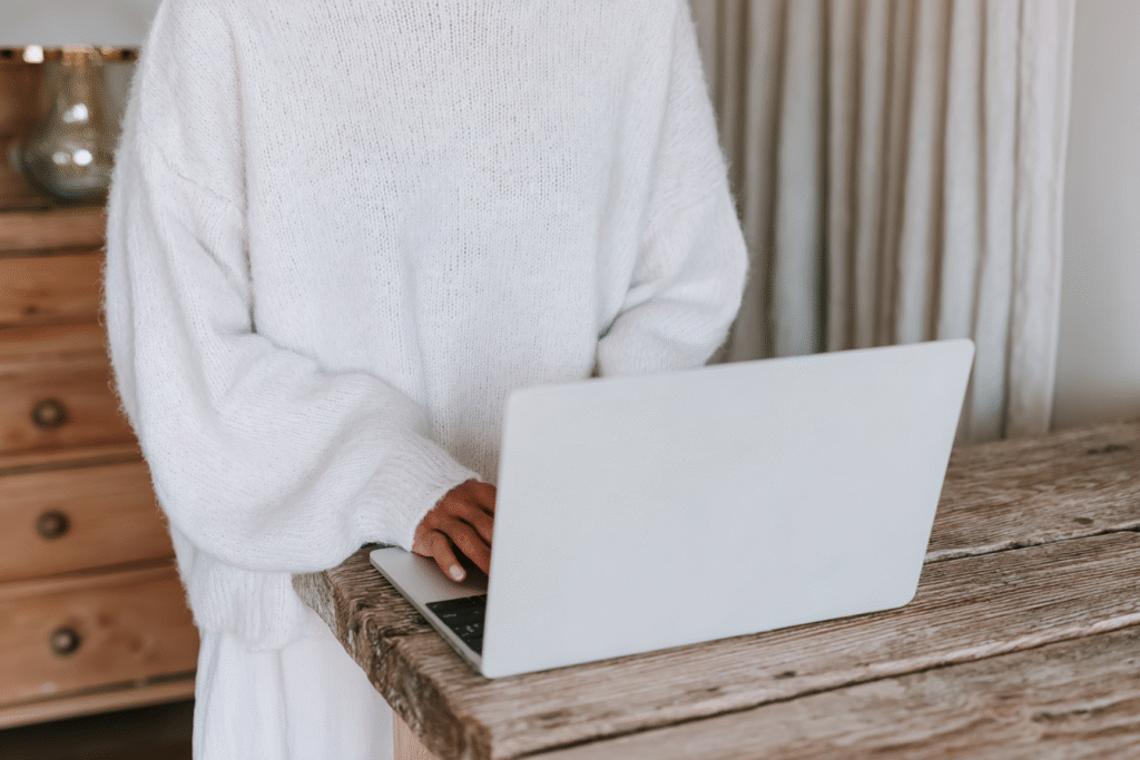 a woman stands and works on a laptop in an oversized sweatshirt
