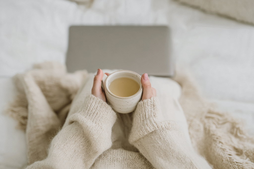 a woman sits with a mug of tea in a cozy sweatshirt and closed laptop