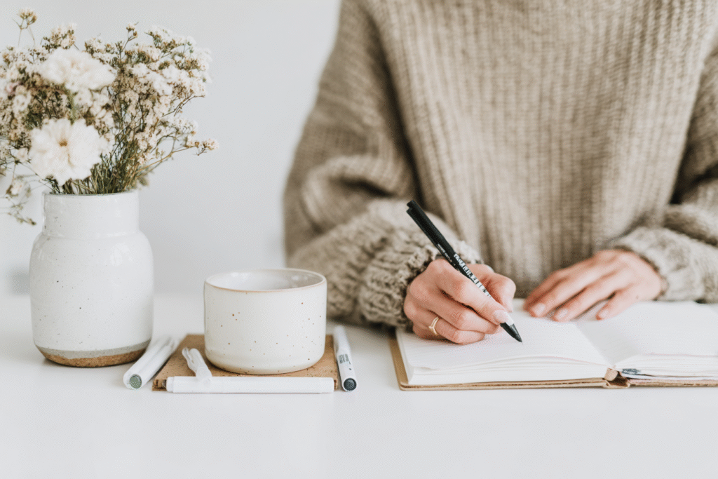 a woman writes in her journal next to a vase of flowers