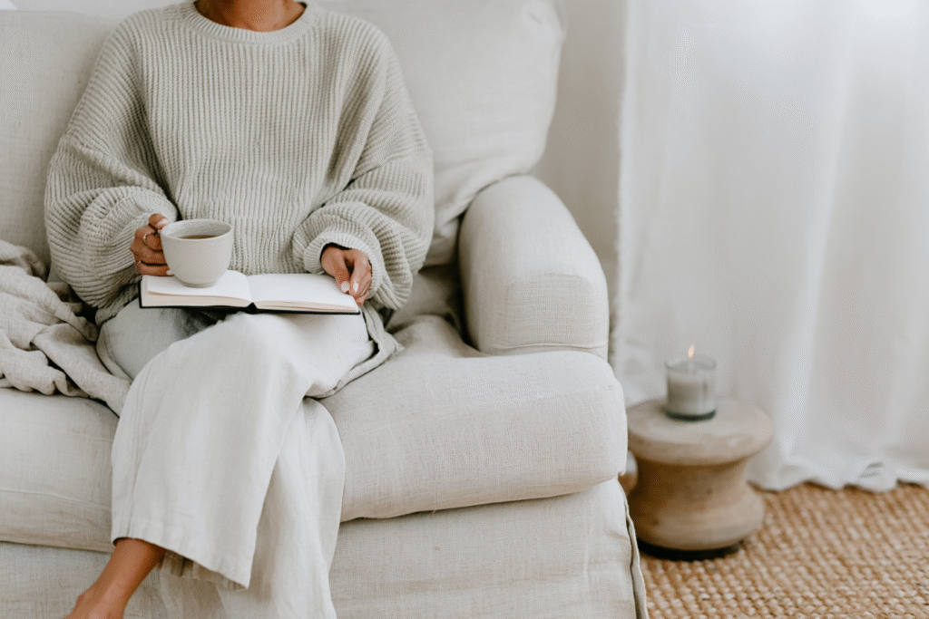 a woman sits on a couch with tea and a planner