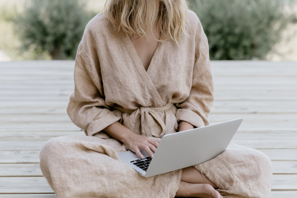 Person in beige robe using a laptop outdoors on wooden deck.