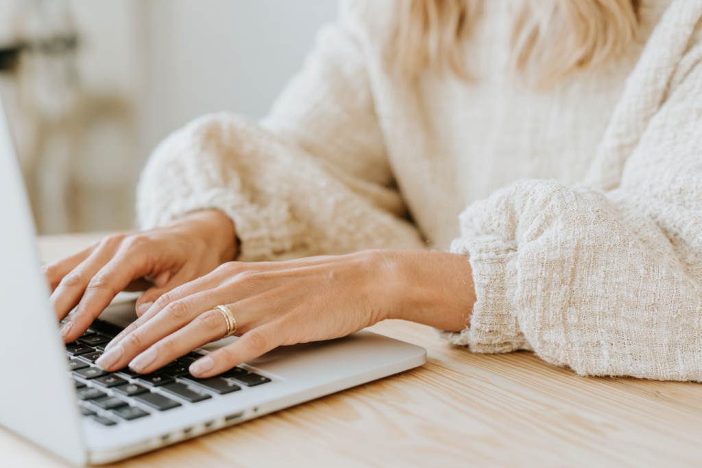 Person typing on a laptop with cozy sweater sleeves, focused on work at a wooden desk.
