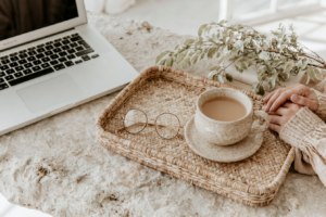 Cozy home office setup with laptop, latte in speckled mug, glasses and greenery on a woven tray, neutral aesthetic